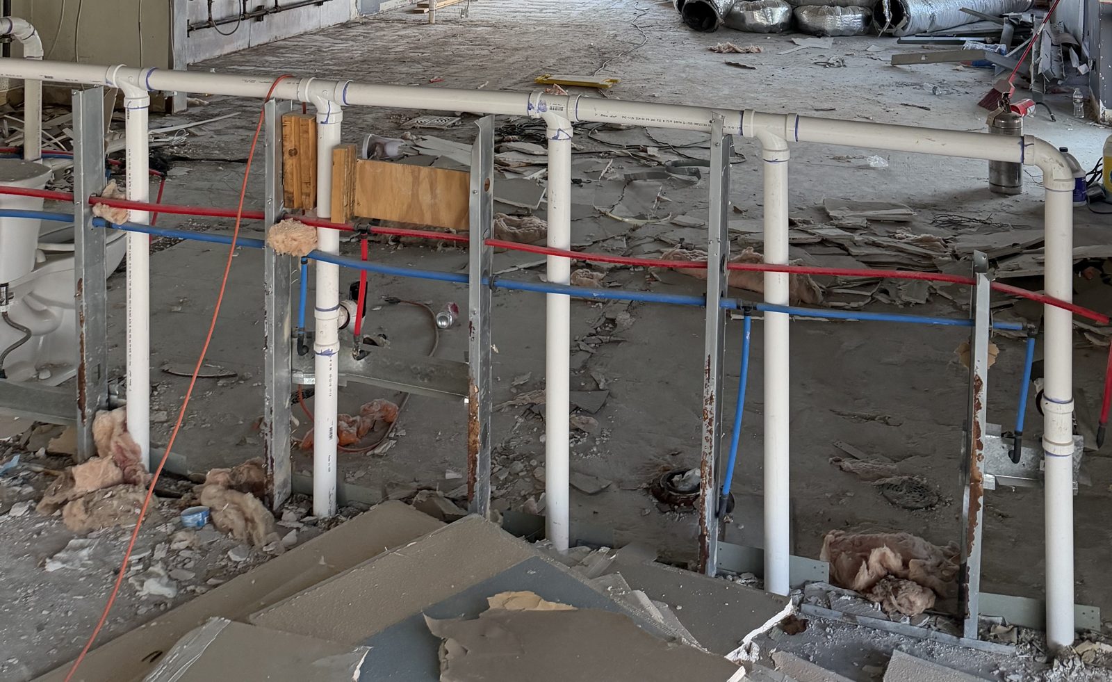 Existing conditions of a gutted retail space with PVC drain lines and red and blue PEX supply lines before a coffee shop tenant improvement in Richardson, TX