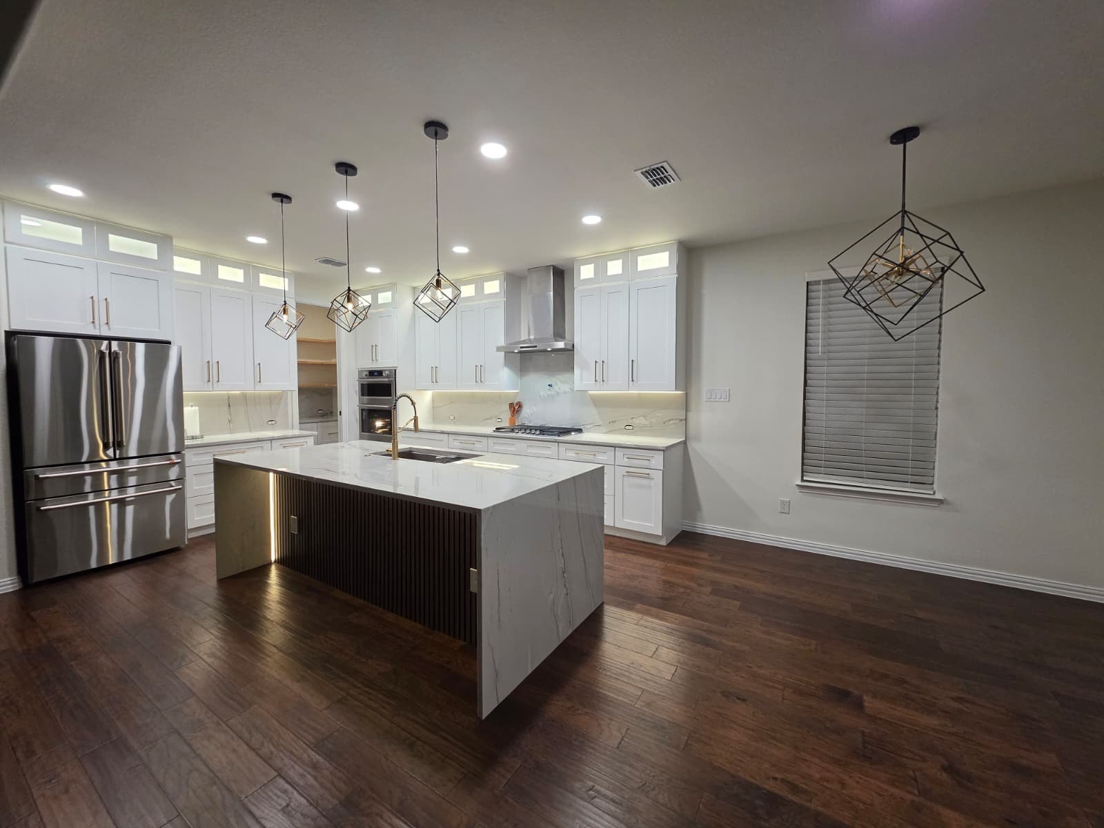 Finished kitchen in Sachse, TX with a waterfall-edge island, fluted wood side panel, white shaker cabinets with brass pulls and geometric pendant lights