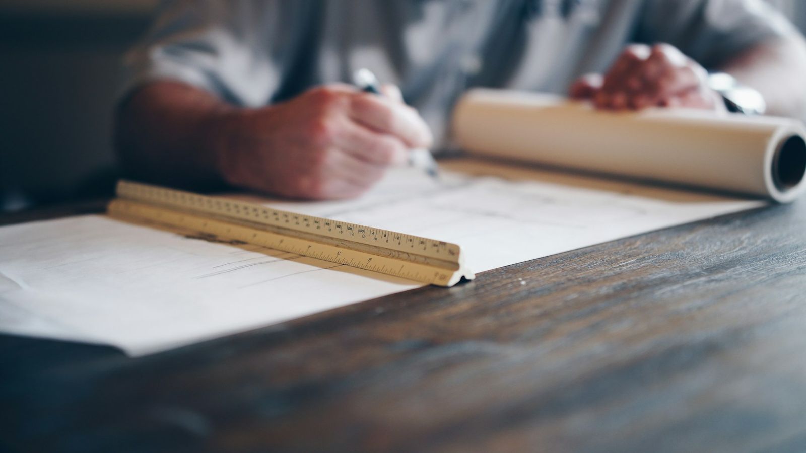 Hands drawing on blueprints with an architect scale ruler